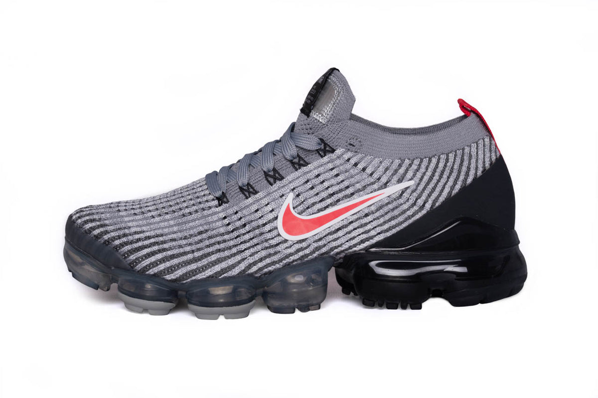 The Nike Air Vapormax Flyknit 3s in a grey and red colourway. This angle showcases the trainer from the side and presents a great view of the Nike swoosh along with the air pods.